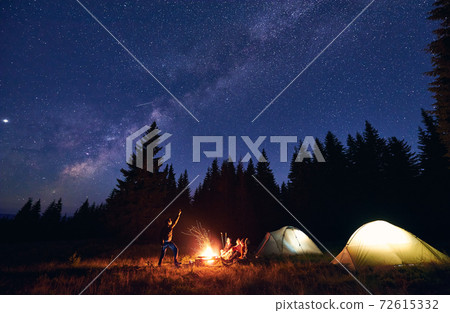 Man is showing his friends Milky Way over tent city. Outdoor recreation 72615332