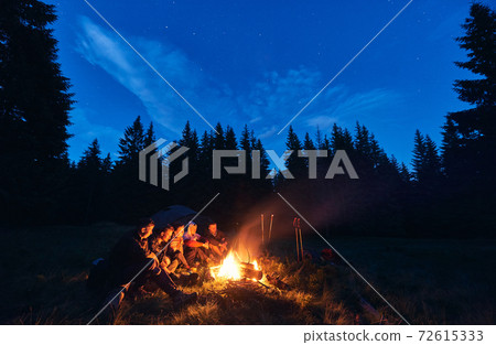 Tourists enjoying time near campfire in forest. Tourists enjoying time near campfire in forest. 72615333