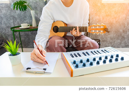 male amateur songwriter playing acoustic guitar and writing a song on white paper in living room male amateur songwriter playing acoustic guitar and writing a song on white paper in living room 72615606