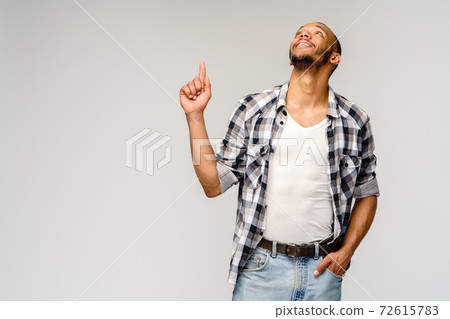 Joyful friendly african-american young man iwearing casual shirt pointing by finger at empty copy space 72615783