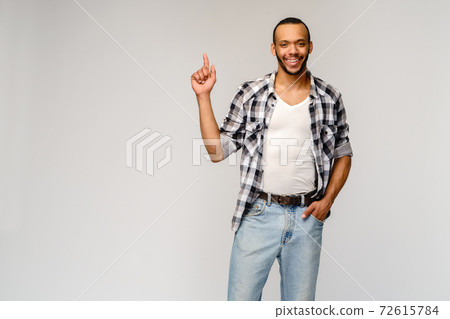 Joyful friendly african-american young man iwearing casual shirt pointing by finger at empty copy space Joyful friendly african-american young man iwearing casual shirt pointing by finger at empty copy space 72615784
