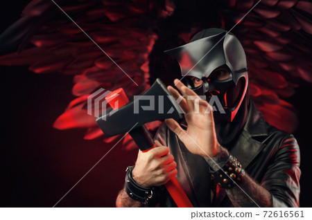a man in a demon skull mask in a leather cloak with an axe on a background of black and red wings a man in a demon skull mask in a leather cloak with an axe on a background of black and red wings 72616561