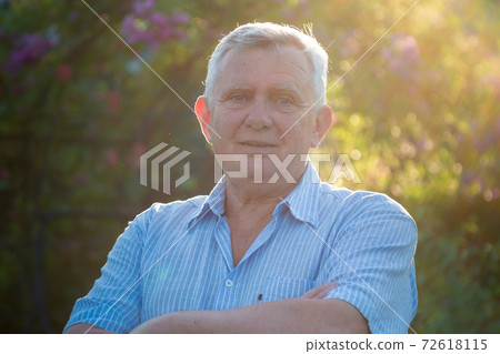 Happy senior man in light blue shirt in sunny garden 72618115