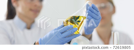 Researcher with glasses holds test tube with marijuana. 72619805