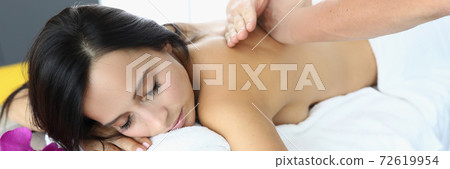 Woman lies with her eyes closed on massage table masseur does back massage Woman lies with her eyes closed on massage table masseur does back massage 72619954