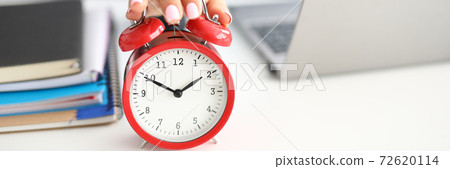 Woman's hand lies on red alarm clock notebooks and laptop lie next to it Woman's hand lies on red alarm clock notebooks and laptop lie next to it 72620114