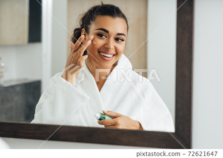 Middle east woman applying cream in bathroom mirror Middle east woman applying cream in bathroom mirror 72621647