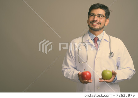 Young handsome bearded Persian man doctor against gray background 72623979
