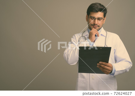 Young handsome bearded Persian man doctor against gray background 72624027