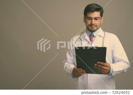 Young handsome bearded Persian man doctor against gray background 72624032