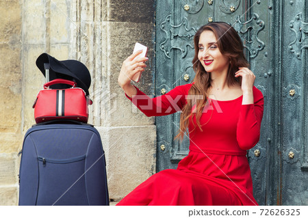 Beautiful tourist girl with a suitcase takes a selfie on the stairs outdoors. Beautiful tourist girl with a suitcase takes a selfie on the stairs outdoors. 72626325