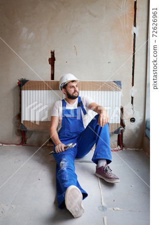Young handsome plumber after installing water radiator in unfinished apartment Young handsome plumber after installing water radiator in unfinished apartment 72626961
