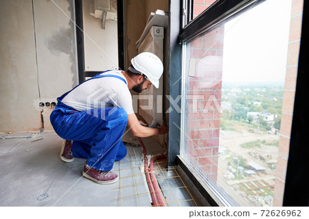Man plumber installing radiator in apartment. Man plumber installing radiator in apartment. 72626962