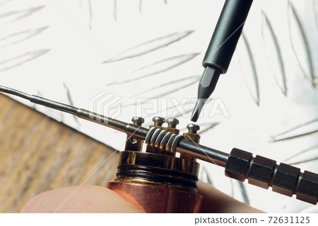 Specialist replaces spring for smoking vape.Professional maintaining electronic cigarette in shop.Fix broken vaping device and quit smoking nicotine cigarettes. Specialist replaces spring for smoking vape.Professional maintaining electronic cigarette in shop.Fix broken vaping device and quit smoking nicotine cigarettes. 72631125