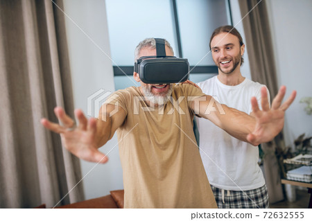 Man in vr glasses walking in the room, his partner supporting him 72632555