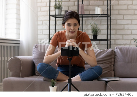 Inspired young woman blogger sitting cross-legged on sofa recording content 72634403