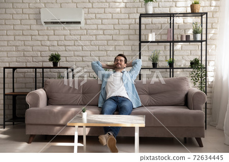 Serene young guy enjoying breathing cool fresh air using conditioner Serene young guy enjoying breathing cool fresh air using conditioner 72634445