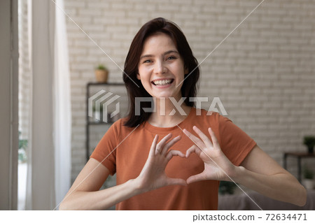 Romantic young lady looking at camera uniting fingers in heart 72634471