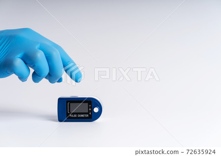Pulse oximeter on a white background. A hand in a medical glove holds a device for health diagnostics 72635924