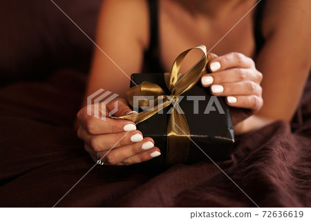 The woman opens a gift in a black box with a gold ribbon The woman opens a gift in a black box with a gold ribbon 72636619