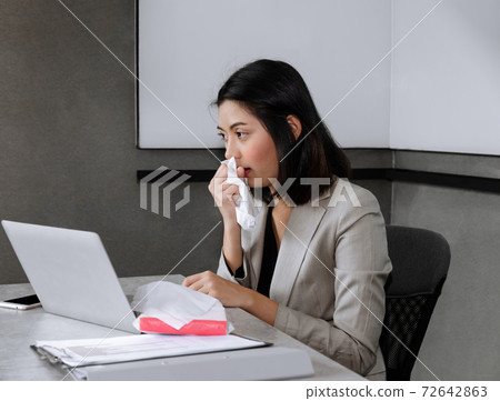Sick bussinesswoman sitting at office desk with laptop, sneezing and coughing in facial tissue while working in meeting room. Working and influenze virus concept. 72642863