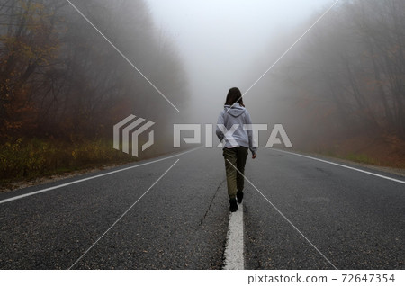 Young woman traveler, rear view on foggy road in autumn forest Young woman traveler, rear view on foggy road in autumn forest 72647354