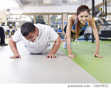 an overweight young man doing push-ups together with a young lady 72647672
