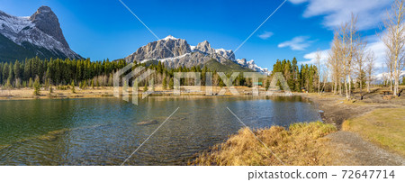 Quarry Lake park lakeshore in late autumn season sunny day morning. Snow capped Mount Rundle and Mount Lawrence Grassi Ha Ling Peak in with blue sky in the background. Canmore, Alberta, Canada. Quarry Lake park lakeshore in late autumn season sunny day morning. Snow capped Mount Rundle and Mount Lawrence Grassi Ha Ling Peak in with blue sky in the background. Canmore, Alberta, Canada. 72647714