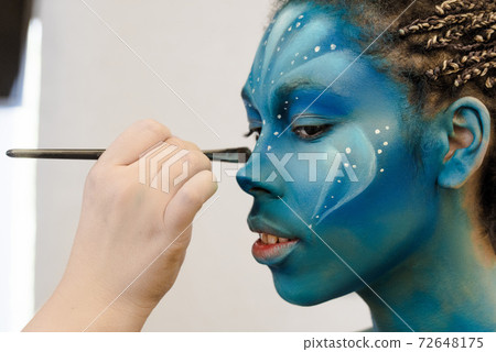 Makeup Artist applies ye shadows to a beautiful woman in Avatar style 72648175