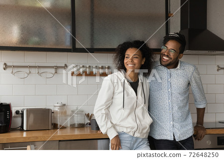 Happy biracial couple dreaming in new home kitchen Happy biracial couple dreaming in new home kitchen 72648250