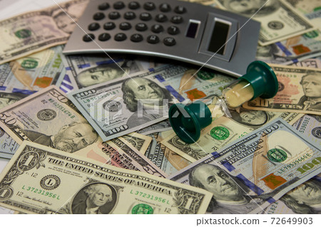 Calculator and hourglass lies on the dollars. 72649903