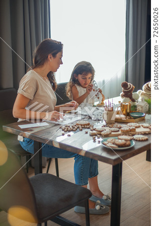 Little cute girl and young beautiful woman cut snowflakes from white paper. Gingerbread and cocoa with marshmallows. Little cute girl and young beautiful woman cut snowflakes from white paper. Gingerbread and cocoa with marshmallows. 72650026