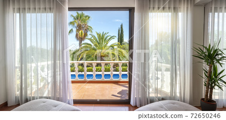 Luxurious view from the living room with sofa to the terrace with pool and garden with palm trees. Luxurious view from the living room with sofa to the terrace with pool and garden with palm trees. 72650246
