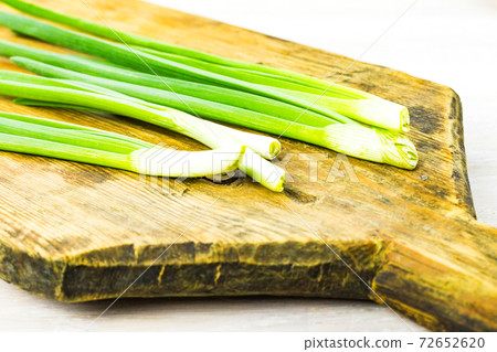 Green spring onion feathers on old wooden cutting board on white table background Green spring onion feathers on old wooden cutting board on white table background 72652620