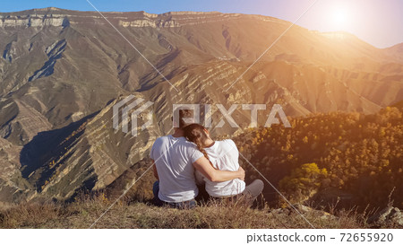 Man and woman hug on hill with dry grass against mountains 72655920