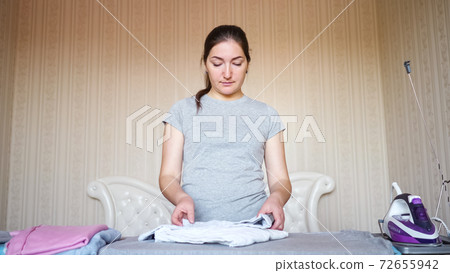Relaxed dark haired housewife stacks clothes after ironing Relaxed dark haired housewife stacks clothes after ironing 72655942