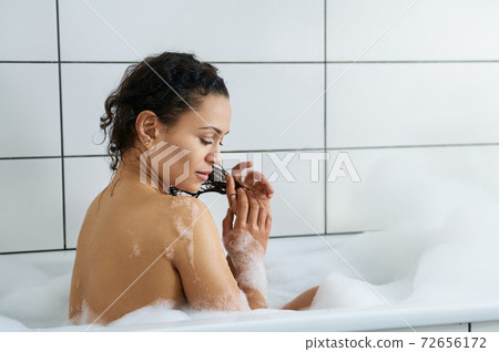 Sise view of a beautiful woman relaxing in bathtub and washinh her curly hair Sise view of a beautiful woman relaxing in bathtub and washinh her curly hair 72656172