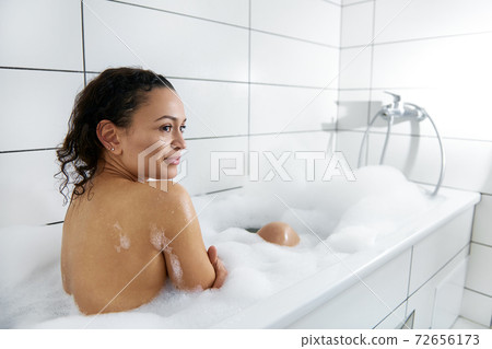 Concept of body care and enjoyment at home.Side view of a young woman taking a bubble bath with foam at home 72656173
