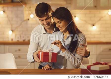 Young happy brunette woman unpacking holiday present from her smiling boyfriend Young happy brunette woman unpacking holiday present from her smiling boyfriend 72660354