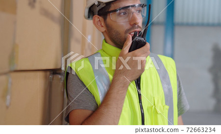 Professional cargo worker talks on portable radio to contact another worker Professional cargo worker talks on portable radio to contact another worker 72663234