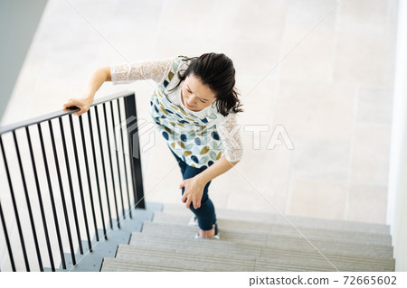 A woman who has a pain in her knees and has difficulty climbing stairs 72665602
