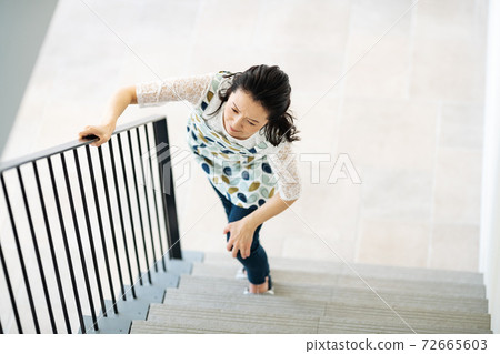 A woman who has a pain in her knees and has difficulty climbing stairs 72665603