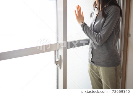 A woman leaning against the window of a room and looking out 72669540