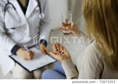 Close-up woman-patient holding pills near her doctor, time to take medications, cure for headache or remedy pain killer drugs. Stay at home concept during Coronavirus pandemic and self isolation Close-up woman-patient holding pills near her doctor, time to take medications, cure for headache or remedy pain killer drugs. Stay at home concept during Coronavirus pandemic and self isolation 72671953