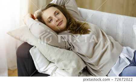 Happy blond woman put hands behind head sitting leaned on couch caucasian female enjoy lazy weekend or vacation in sunny living room 72672022