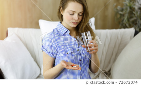 Young woman holding pills time to take medications, cure for headache, high blood pressure or cholesterol level remedy pain killer drugs Young woman holding pills time to take medications, cure for headache, high blood pressure or cholesterol level remedy pain killer drugs 72672074