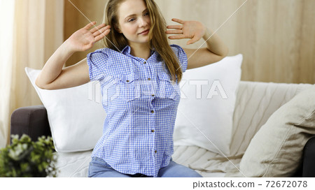 Happy blond woman put hands behind head sitting leaned on couch caucasian female enjoy lazy weekend or vacation in sunny living room 72672078