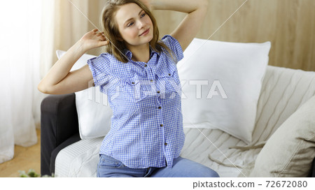 Happy blond woman put hands behind head sitting leaned on couch caucasian female enjoy lazy weekend or vacation in sunny living room 72672080