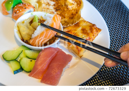 Closeup photo of human hands using chopsticks while eating sushi Closeup photo of human hands using chopsticks while eating sushi 72673329