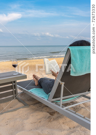 Traveller reading book with glass of wine on beautiful beach Traveller reading book with glass of wine on beautiful beach 72673330